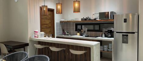 Une cuisine moderne dotée d’un îlot central, de tabourets de bar, d’un réfrigérateur et de luminaires suspendus.
