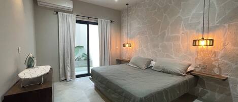 Un dormitorio con cama, ventilador de techo, mesita de noche, tabla de planchar y pared de piedra.