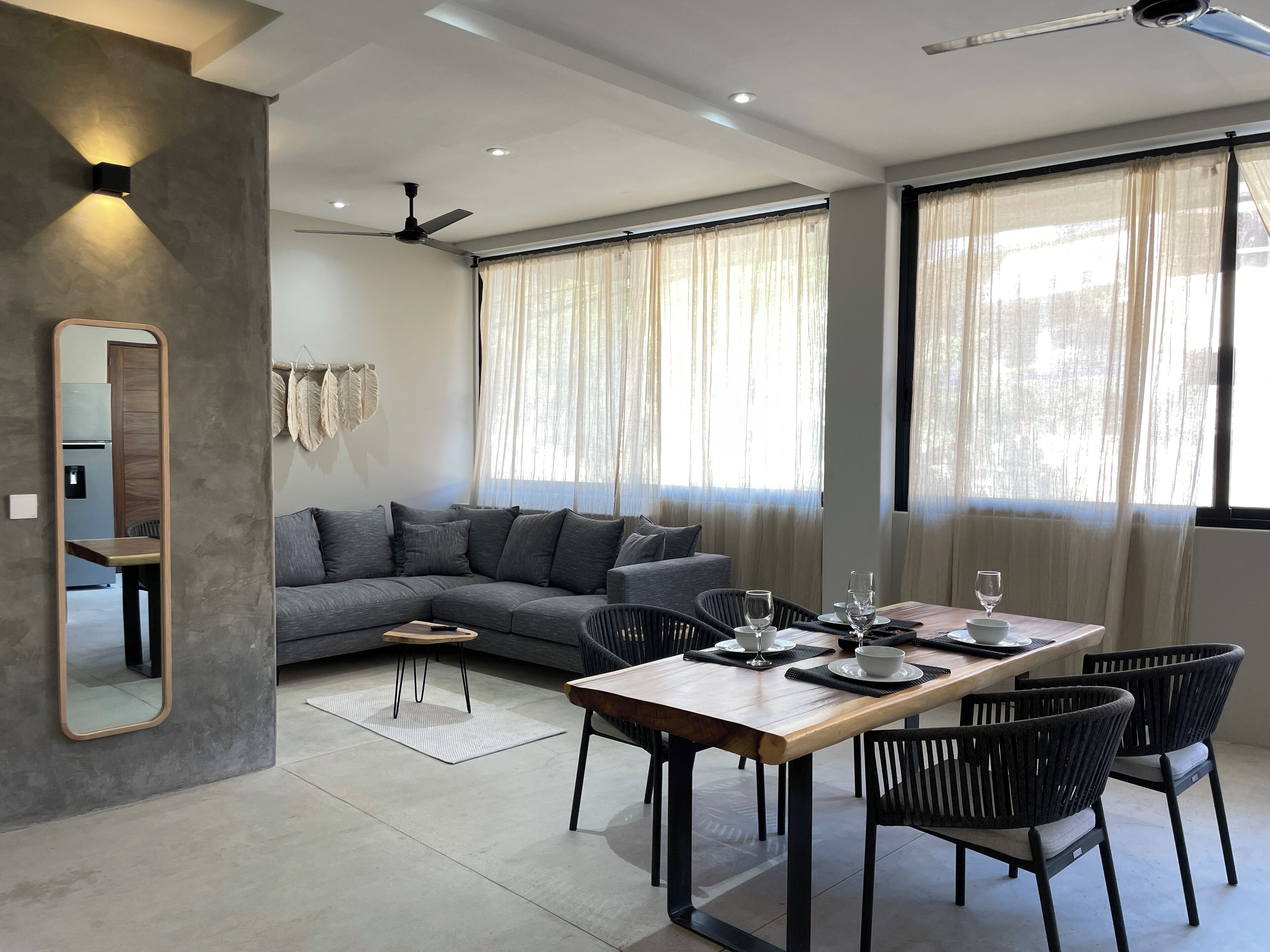 A modern living room with a grey sectional sofa, a wooden dining table with chairs, and a ceiling fan.