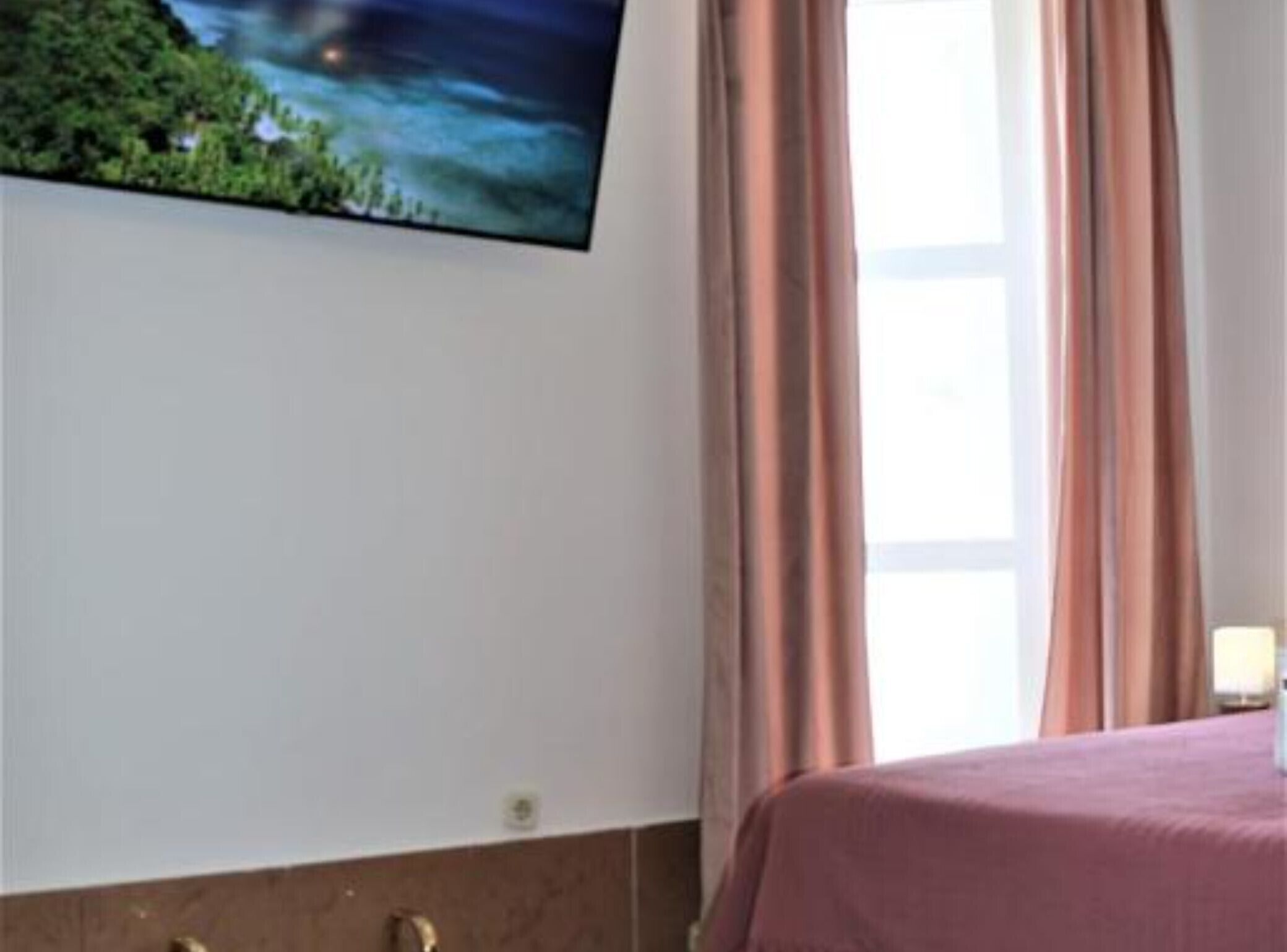Hotellihuone, jossa on sänky, seinälle asennettu televisio ja ikkuna, jossa on verhot.