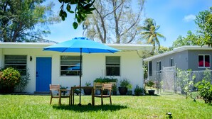 Une maison avec une porte bleue, une terrasse avec une table et des chaises, et un parasol bleu.