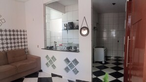 A living room with a checkered floor, a sofa, and a kitchen area with a tiled backsplash and a coffee maker. - Charming 3 bedroom house COP (Umarizal Belém)