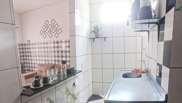 A kitchen with a black and white checkered floor, a stainless steel sink, and a potted plant on a shelf. - Charming 3 bedroom house COP (Umarizal Belém)