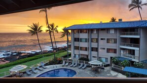 A hotel with a swimming pool, lounge chairs, and a view of the ocean at sunset.