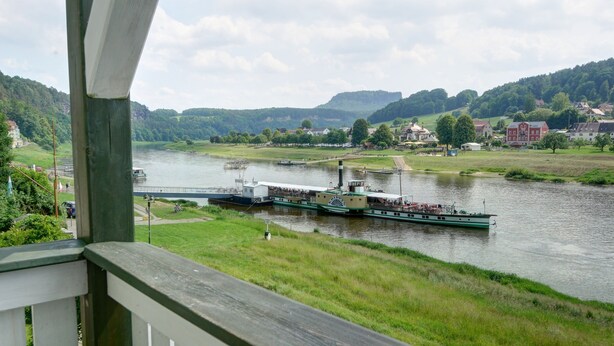 Une rivière avec un bateau amarré à un quai, entourée de verdure et avec des bâtiments en arrière-plan.