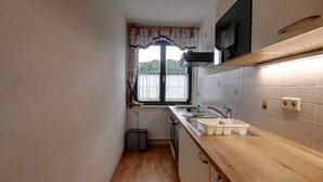 Une cuisine de taille réduite, dotée d’une fenêtre, d’un radiateur, d’un évier et d’un four à micro-ondes.