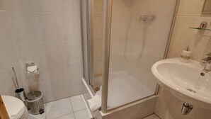 Une salle de bain avec une douche à parois de verre, un lavabo, des toilettes et une poubelle.