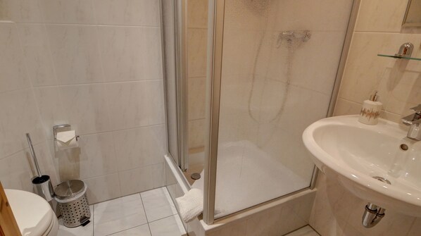 A bathroom with a glass shower enclosure, a sink, a toilet, and a trash can.