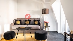 Ein modernes Wohnzimmer mit einem grauen Sofa, schwarzen Hocker, einem runden Couchtisch und einer stehenden Stehlampe.