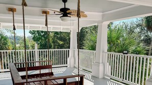 Eine überdachte Veranda mit einer hölzernen Hängematte, weißen Geländern und einem Deckenventilator.
