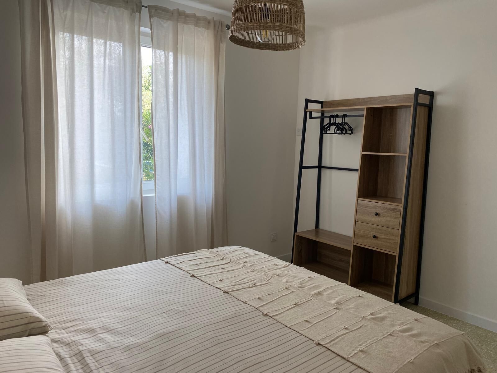 Une chambre à coucher avec un lit, une armoire en bois et une fenêtre ornée de rideaux légers.