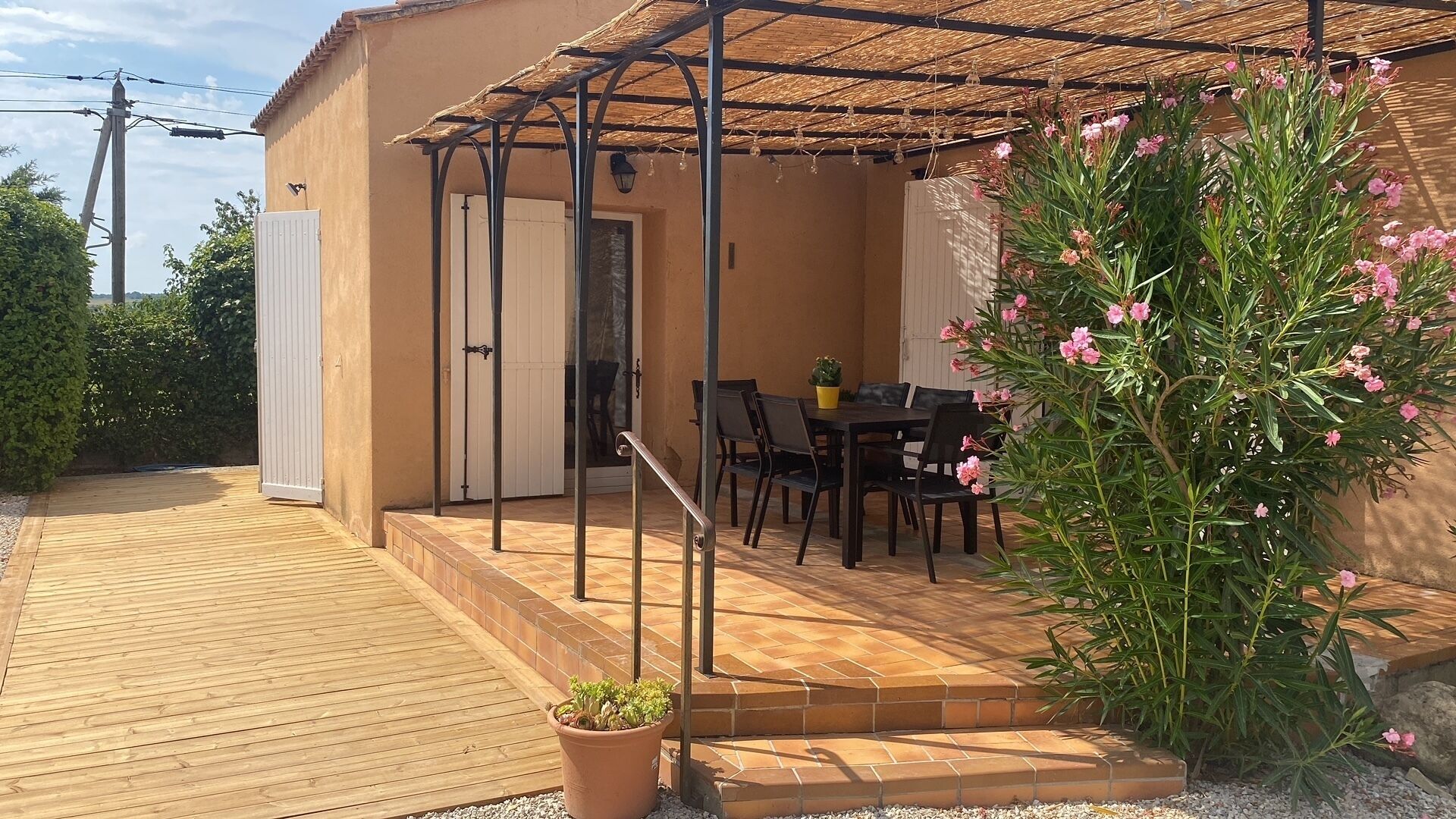 A covered patio with a wooden deck, a table with chairs, and a potted plant.