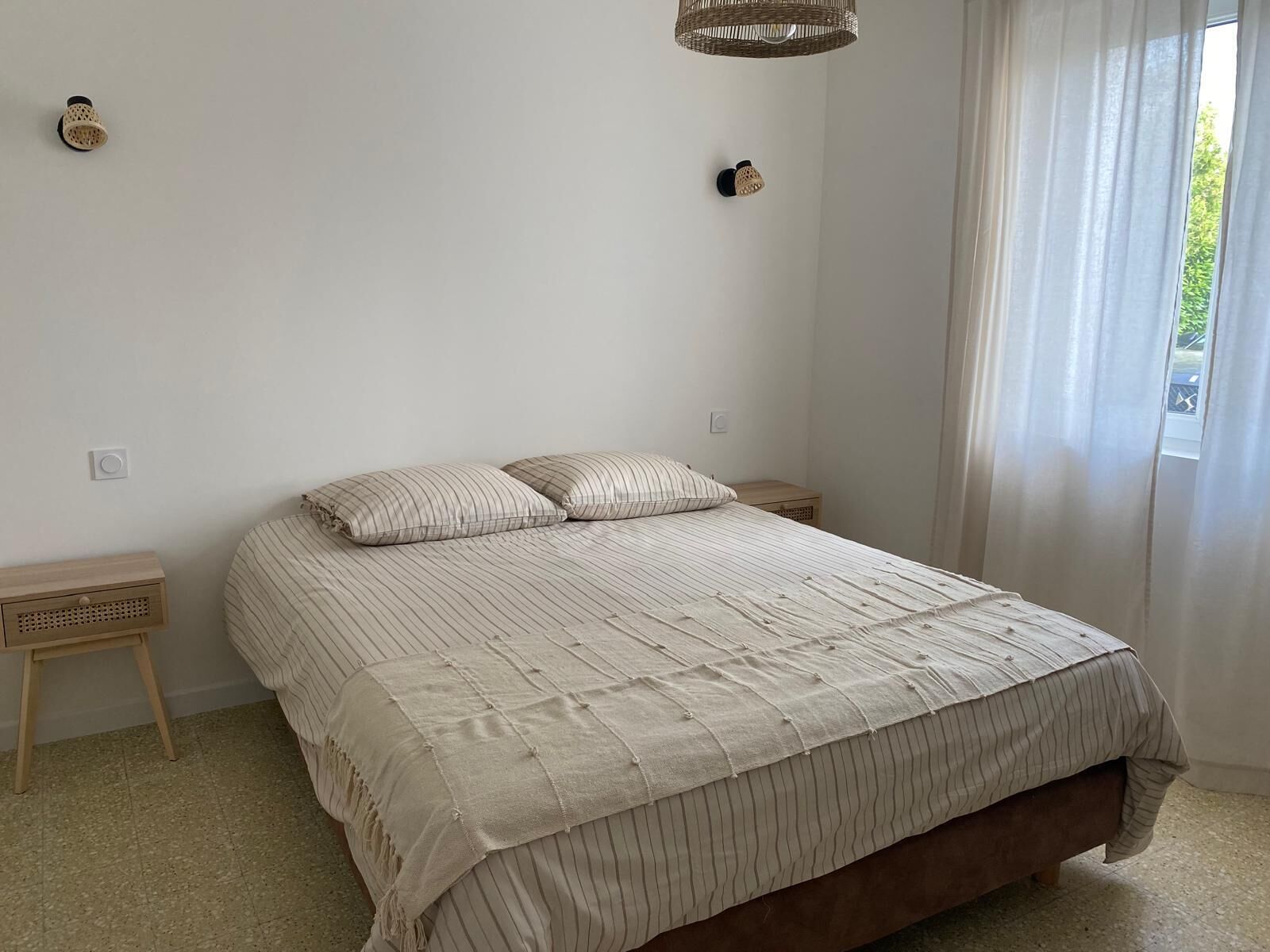 A bedroom with a bed, a nightstand, a lamp, and a window with curtains.