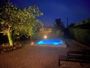 A swimming pool with a stone border, surrounded by gravel, trees, and a bench. - Marinette's house (Séguret)