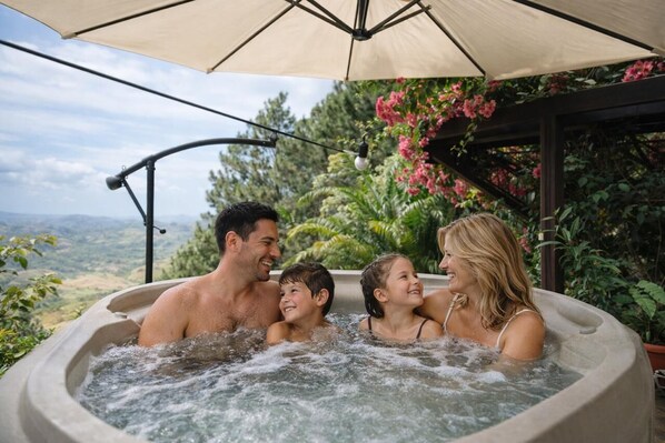 Un jacuzzi con vistas al paisaje, rodeado de vegetación y una pérgola.