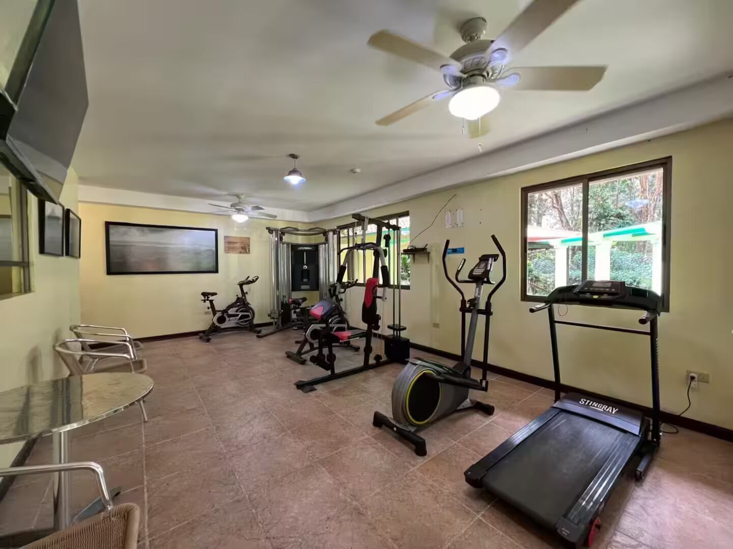 Une salle de sport équipée de matériel d’exercice, d’un tapis de course et d’un ventilateur de plafond.