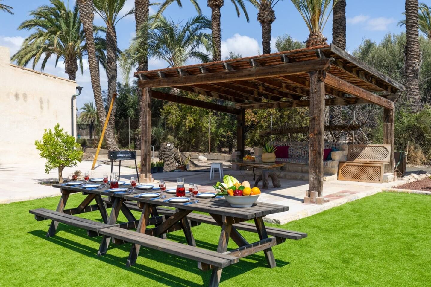 An outdoor patio with a wooden pergola, picnic tables, and a stone wall.