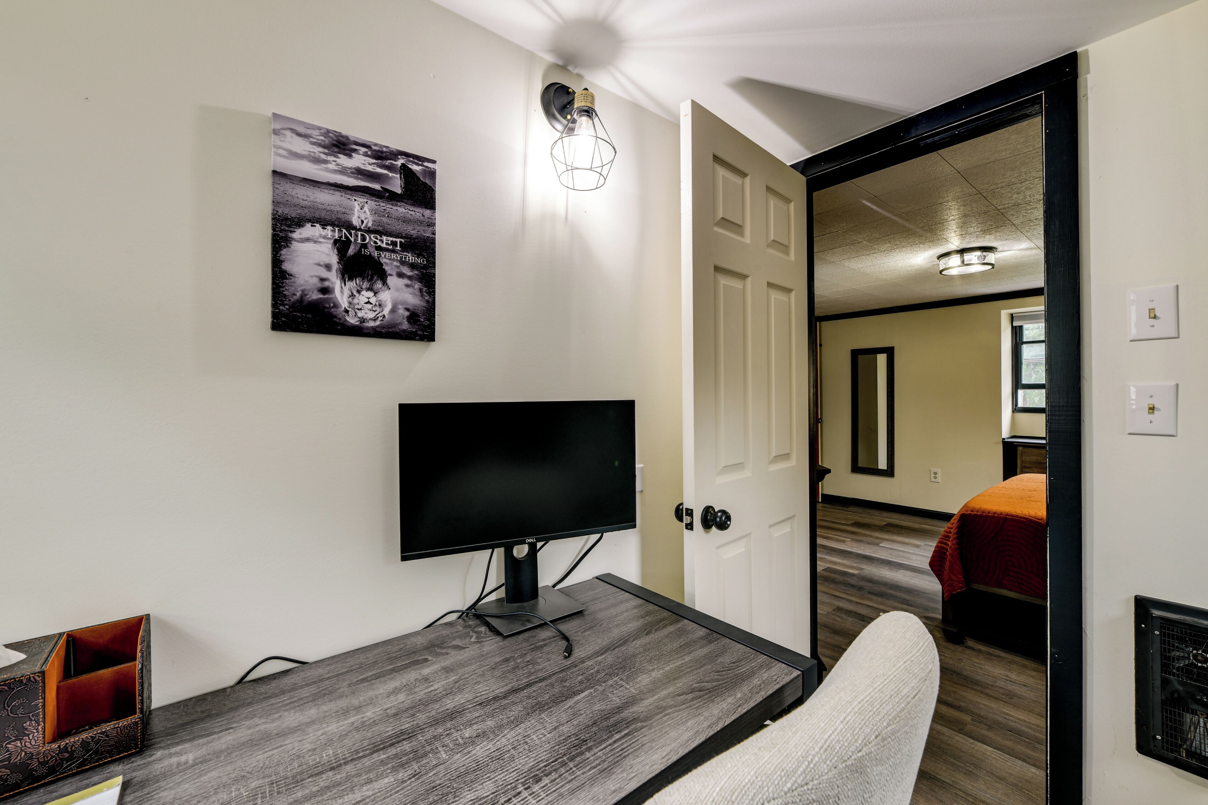Habitació moderna amb escriptori de fusta, televisió de pantalla plana, quadre al mur i porta que dona a una altra habitació.