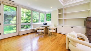 A room with large windows, a round wooden table with four chairs, and built-in white shelving. - 18 Mi to Boston - Stylish Unit in Upscale Enclave! (Weston)