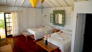 A room with two beds, a wooden bench, a small table with a vase, and a green-framed mirror. - Barefoot Suites (Ratho Mill)