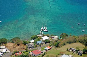An aerial view of a coastal area with clear turquoise waters, several boats docked at a pier, and a small settlement with houses and buildings. - Barefoot Suites (Ratho Mill)