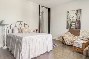 Un dormitorio con cama, mesita de noche, lámpara, sillón, sofá y un cuadro en la pared.
