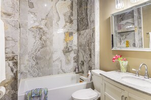 Un baño con bañera, inodoro, lavamanos y paredes de mármol.