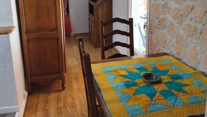 A dining area with a wooden table, chairs, and a quilted table runner. A wooden cabinet and a small wooden shelf are visible in the background. - Charming Provencal country house in the heart of the Alps de Haute Provence 3*. (Mézel)