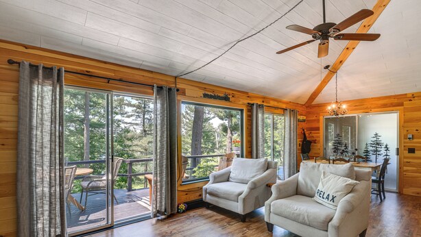 A cozy cabin interior with wooden walls, a ceiling fan, and a balcony with a table and chairs. - Fishing & Boating Paradise: St Lawrence River Home (Hammond)