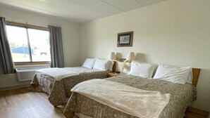 Habitación de hotel con dos camas, un ventanal con cortinas, un cuadro en la pared y suelo de madera.