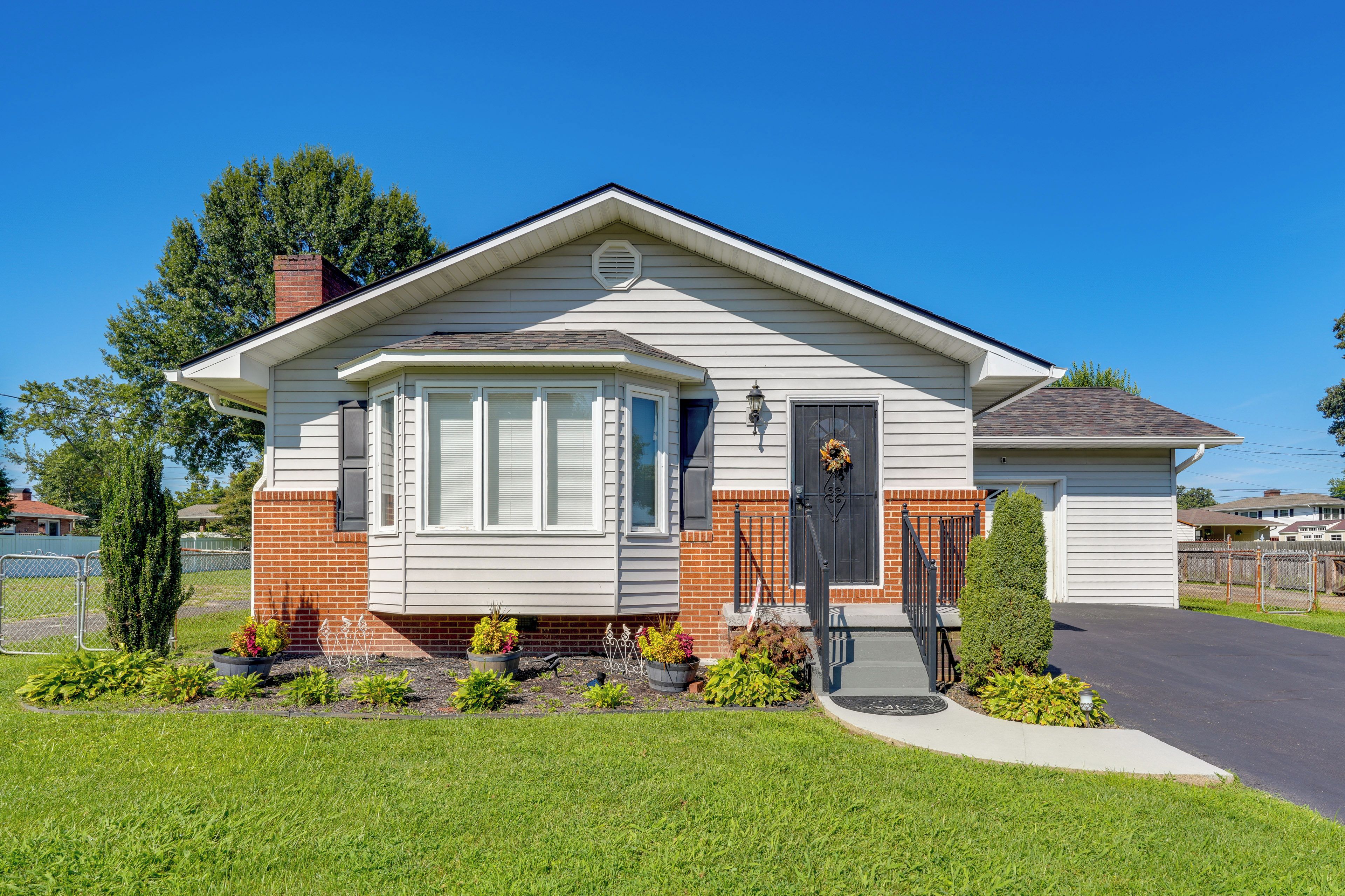 A single-story house with a gabled roof, a front porch, and a small front yard with various plants.
