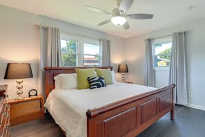 A bedroom with a wooden bed, two bedside tables with lamps, a ceiling fan, and windows with curtains. - Charming Kingsport Home w/ Spacious Fenced Yard! (Kingsport)