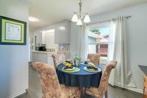 A dining area with a table set for four, chairs with floral upholstery, a chandelier, and a view of the outside through a window with curtains. - Charming Kingsport Home w/ Spacious Fenced Yard! (Kingsport)