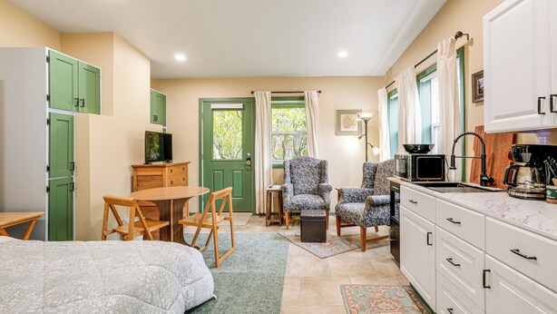 A compact room with a bed, a small table, a chair, a desk, a kitchenette, and a green door. - < 1/2 Mi to OSU: Studio in Corvallis Near Parks (Corvallis)
