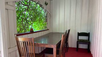 A dining area with a wooden table and chairs, a window with a view of green foliage, and a red carpet.
