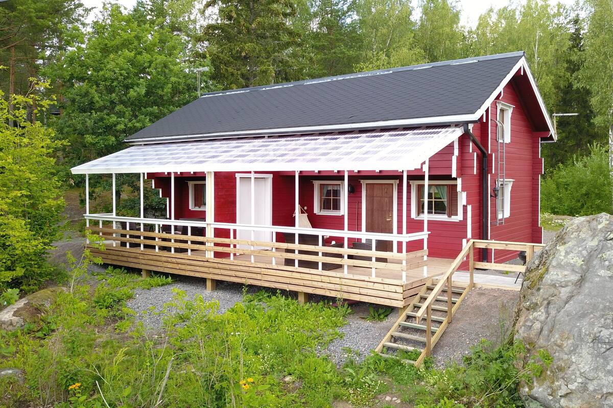 A red cabin with a covered porch and wooden steps leading up to the entrance.