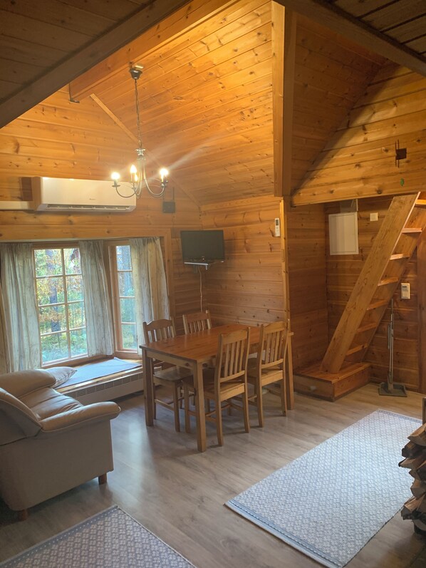 A cozy cabin interior with a dining table, chairs, a sofa, a TV, and a staircase. - Lomahyppäys (Naantali)