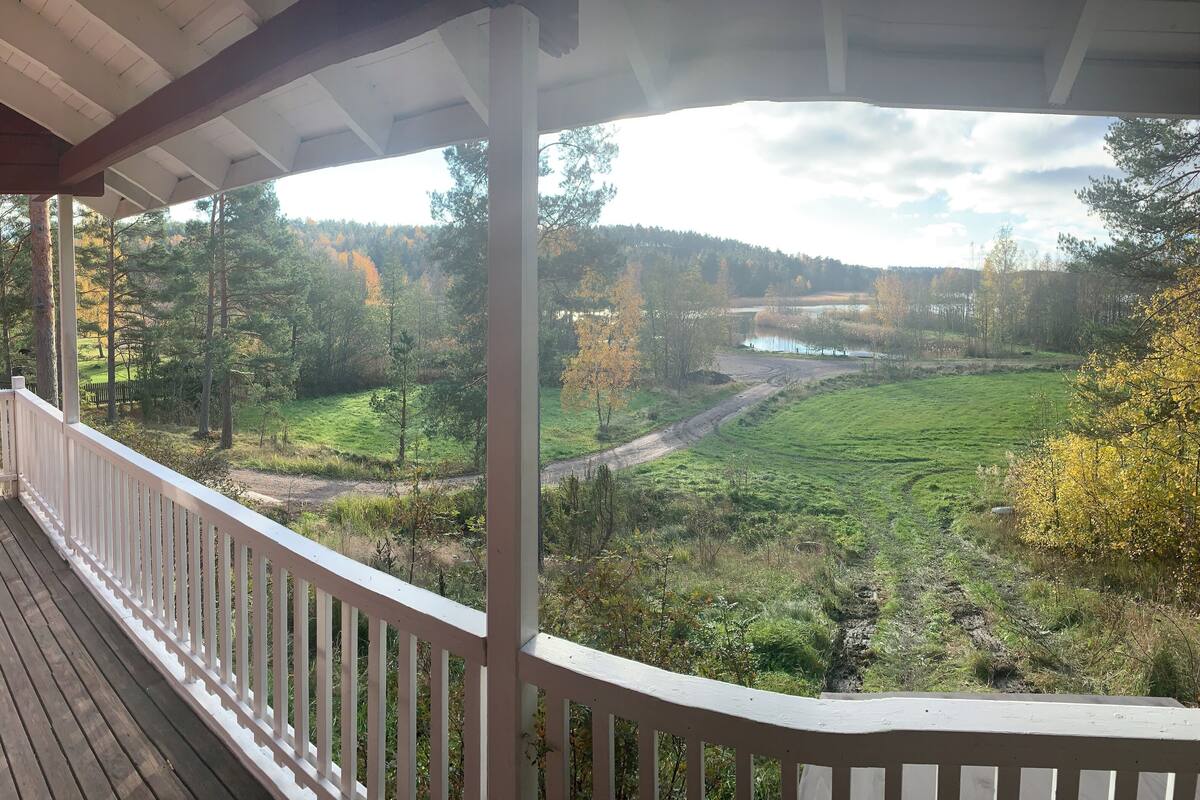 A wooden deck with white railings overlooking a grassy field and a river.
