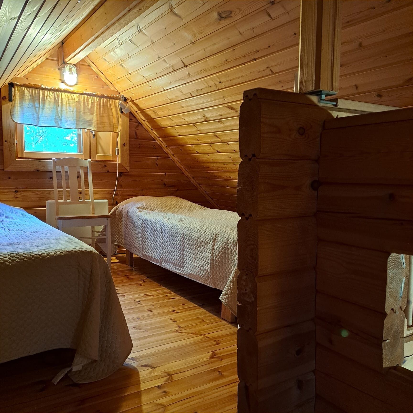 Una habitación de cabaña acogedora con dos camas, una ventana con cortinas y un techo de madera.