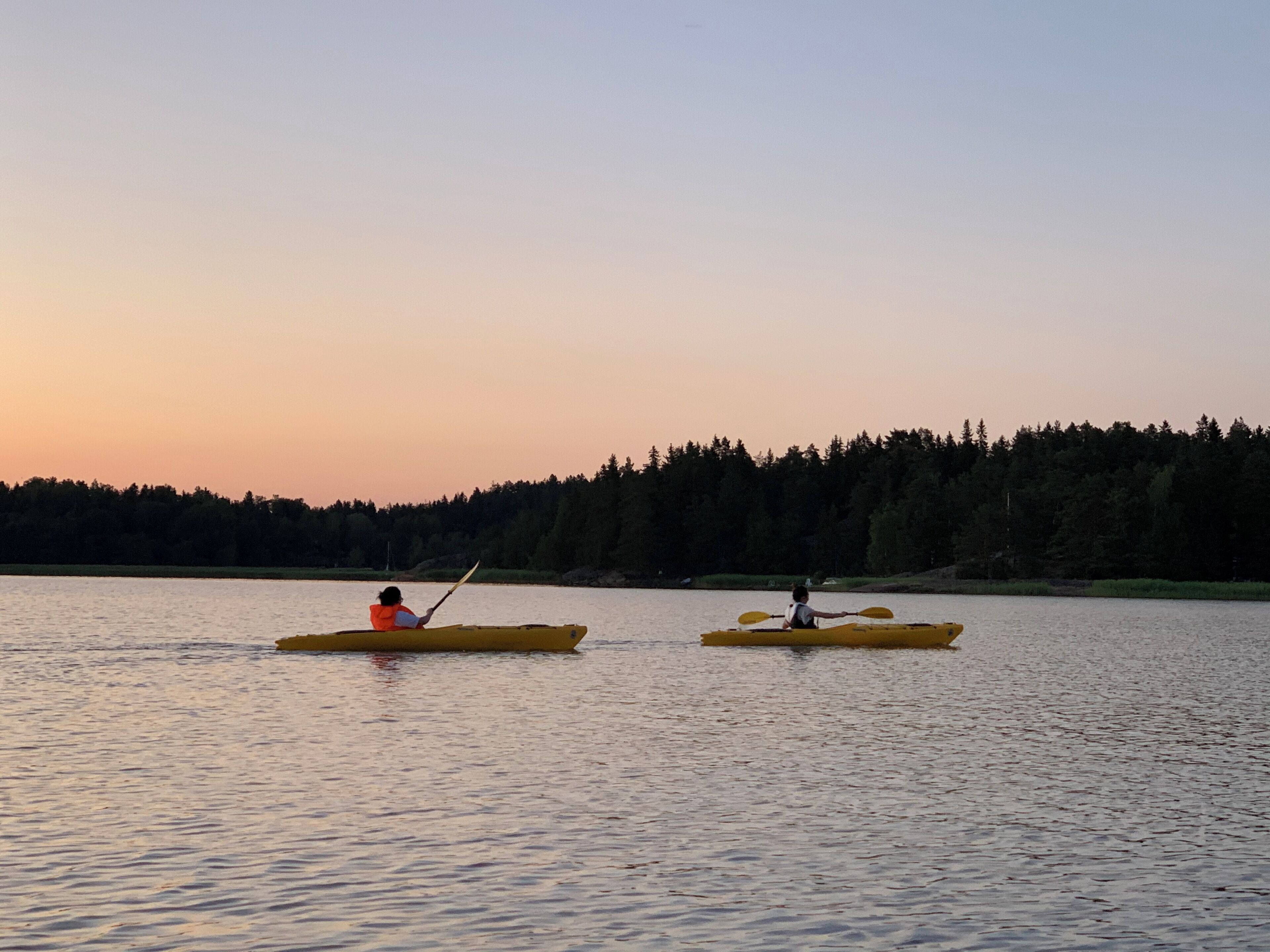 Two kayaks on a calm lake at sunset with a forested shoreline in the background.