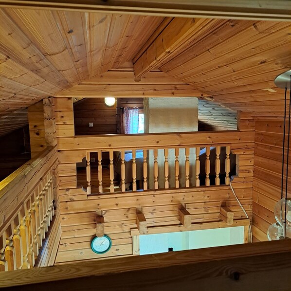 A wooden interior with a balcony, a clock, and a window with curtains.