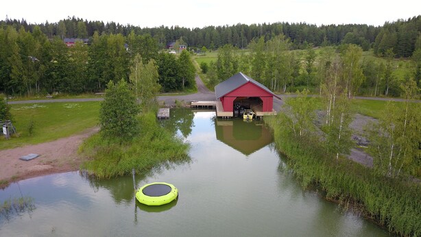 A red building with a covered entrance, surrounded by water and greenery. - Lomahyppäys (Naantali)