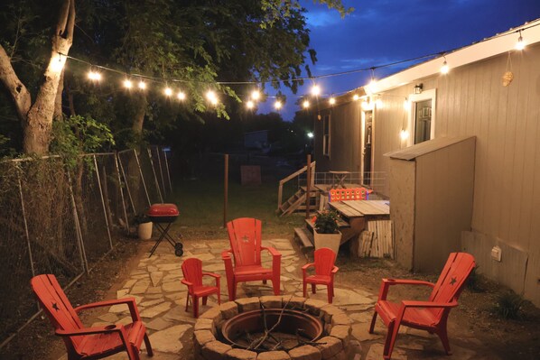 Un patio trasero con un brasero, asientos exteriores y luces colgantes.