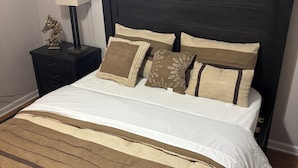 Een bed met een donker hoofdbord, meerdere kussens en een gestreept dekbed.