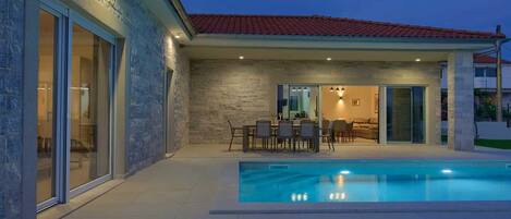 A modern house with a swimming pool, stone exterior, and a dining area with outdoor seating.