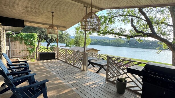Una terraza techada con sillas Adirondack, una parrilla y vistas a un lago.