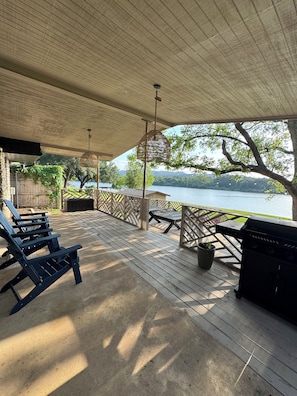 A covered deck with Adirondack chairs, a grill, and a view of a lake.