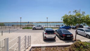 A parking area with cars, a clear sky, and a view of the sea.