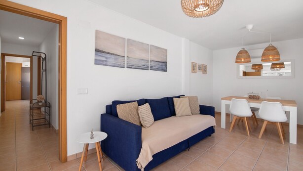 A living room with a sofa, a small round table, and a dining area with chairs.