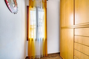 A room with a wooden wardrobe, a window with sheer curtains, and a decorative mirror on the wall. - Vrbo Property (Foligno)